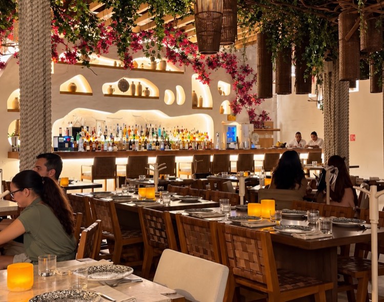 A restaurant with a leafy canopy and woven pendant lamps over dining tables
